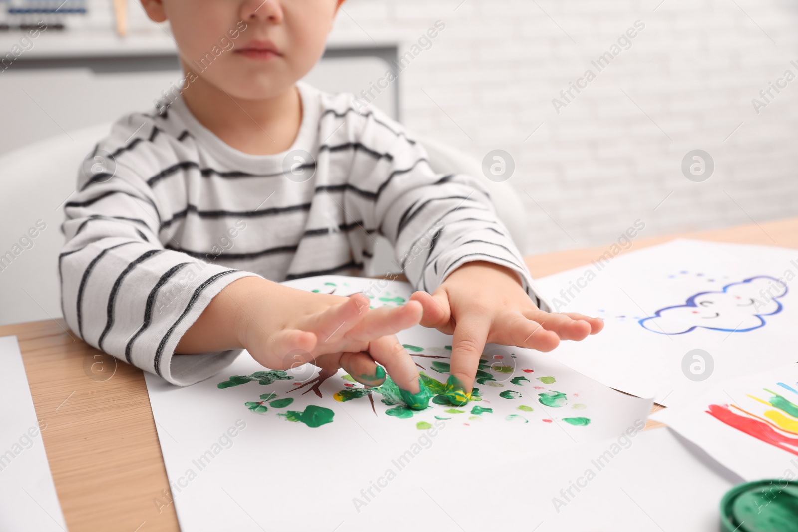 Photo of Little boy painting with fingers at wooden table indoors, closeup