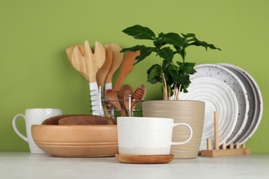 Potted plant and set of kitchenware on white table near green wall. Modern interior design