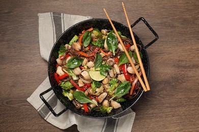 Photo of Stir-fry. Tasty noodles with meat in wok and chopsticks on wooden table, top view