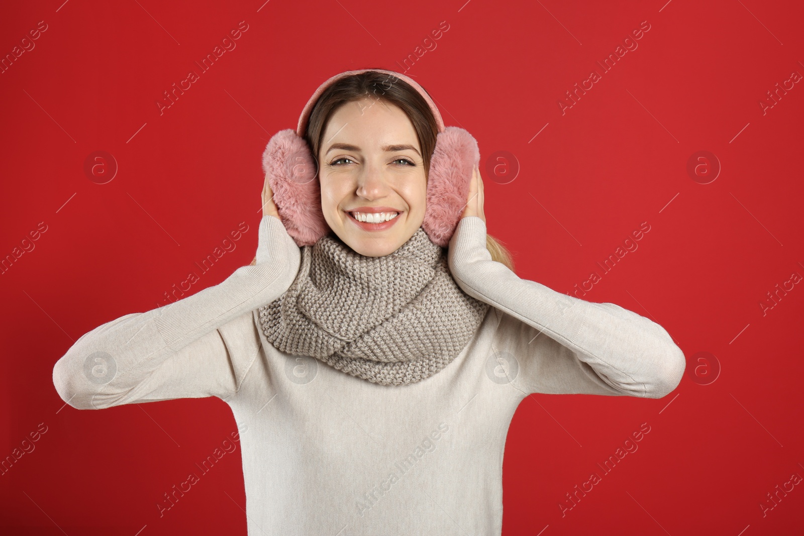 Photo of Happy woman wearing warm earmuffs on red background