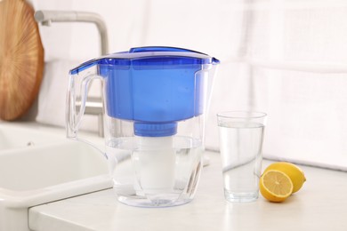 Photo of Water filter jug, glass and lemons on countertop in kitchen