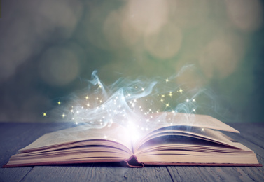 Image of Open book with magic glowing on wooden table. Fairy tale