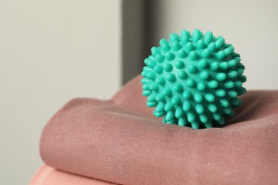 Photo of Turquoise dryer ball on brown soft clothing, closeup