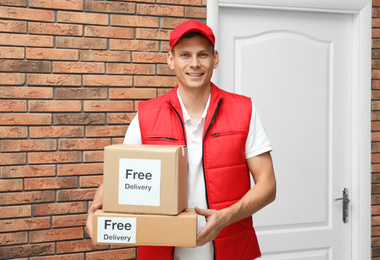 Photo of Courier holding parcels with stickers Free Delivery indoors