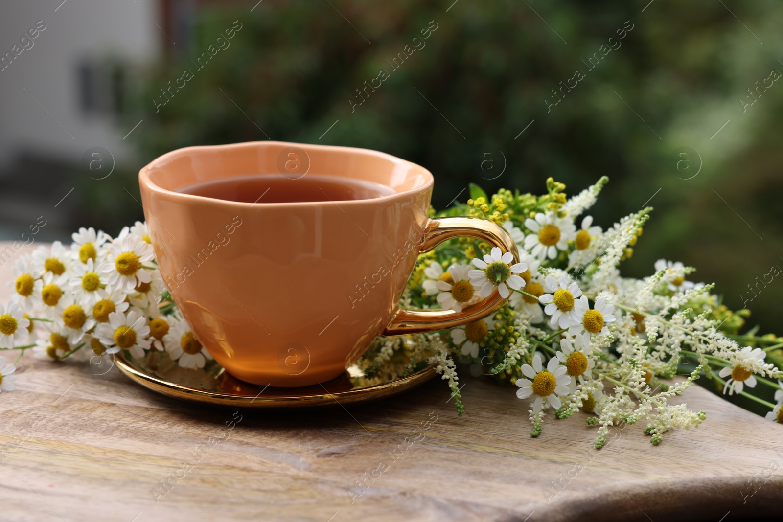 Photo of Cup of delicious chamomile tea and fresh flowers outdoors