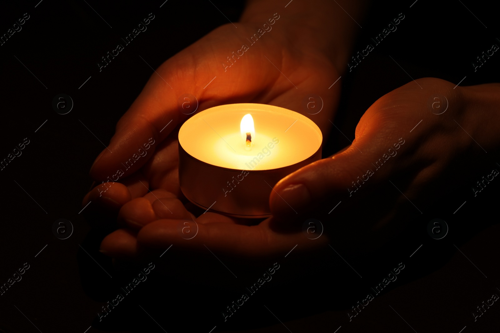 Photo of Woman holding burning candle in hands on black background, closeup