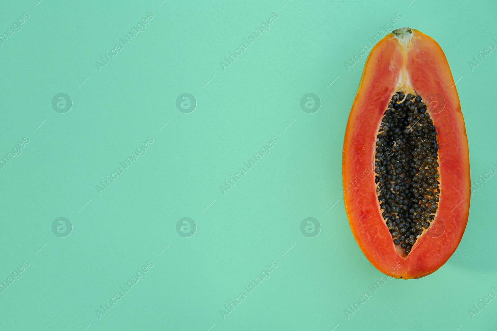 Photo of Half of fresh ripe papaya on light turquoise background, top view with space for text. Exotic fruit