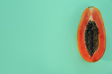 Photo of Half of fresh ripe papaya on light turquoise background, top view with space for text. Exotic fruit