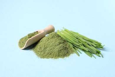 Photo of Pile of wheat grass powder, scoop and fresh sprouts on light blue table