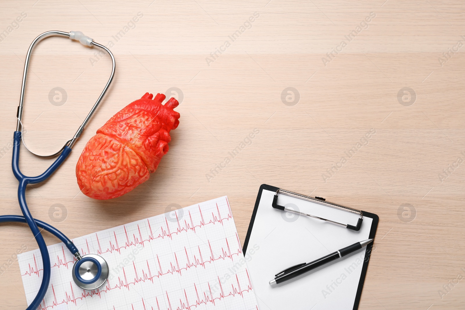 Photo of Stethoscope, cardiogram, clipboard, heart model and space for text on wooden background, flat lay. Cardiology concept