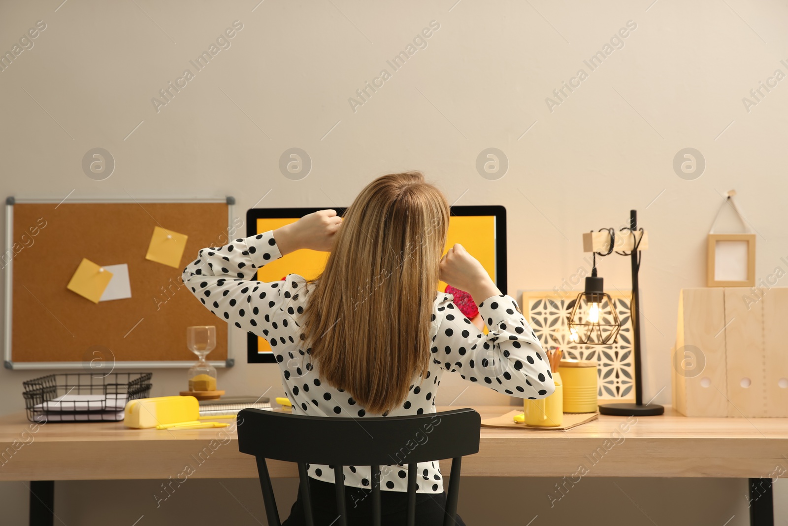 Photo of Woman sitting at wooden desk with computer near light wall, back view. Interior design