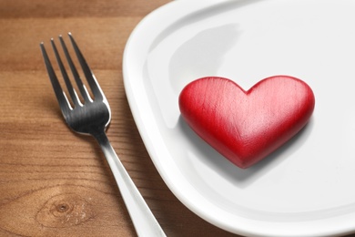 Photo of Plate with red heart and fork on wooden table, closeup. Healthy diet concept