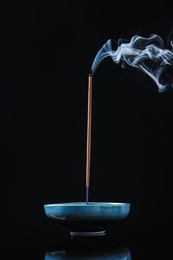 Photo of Incense stick smoldering in holder on black background