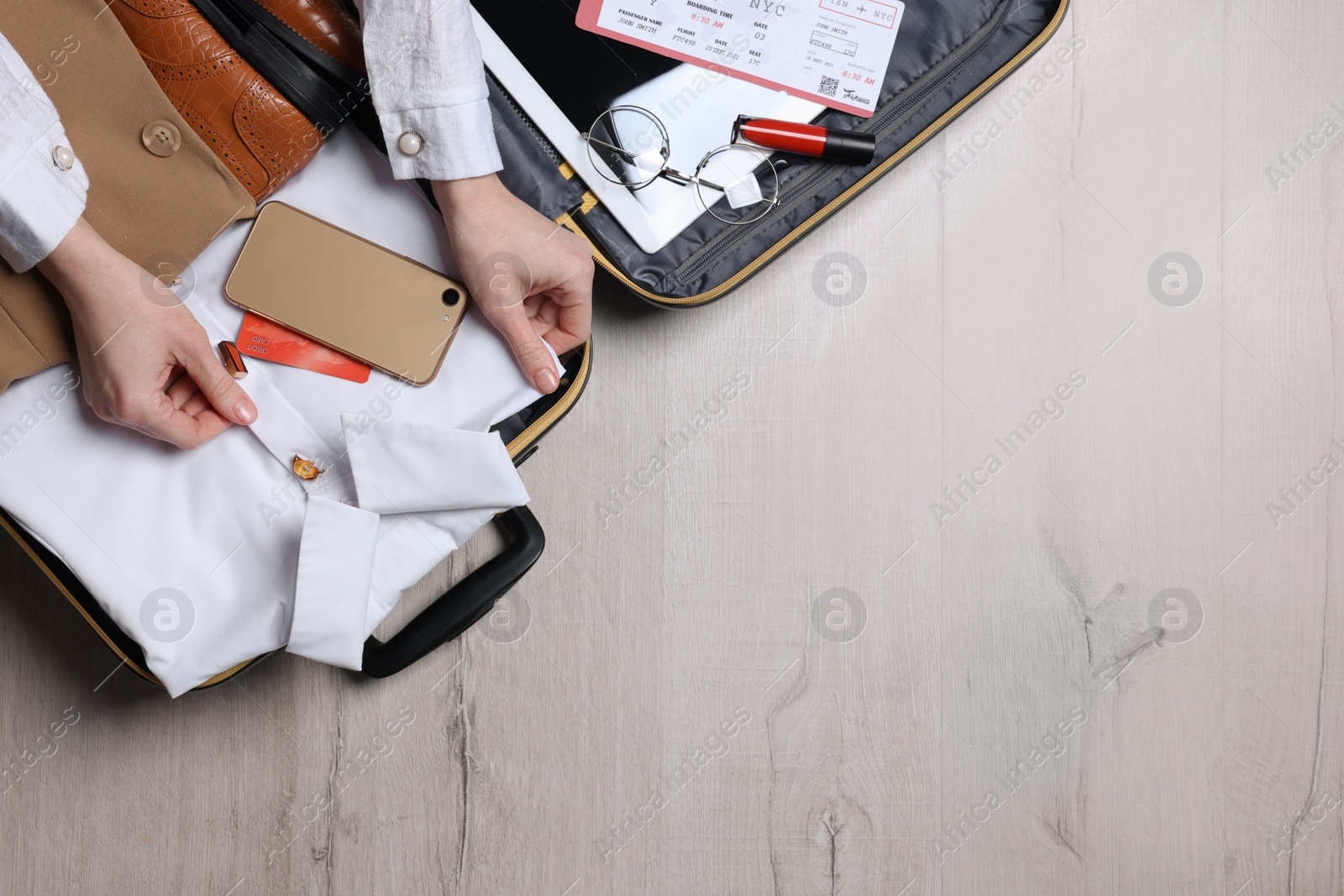 Photo of Woman packing suitcase for business trip on wooden floor, top view