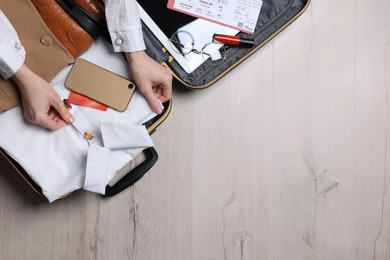 Woman packing suitcase for business trip on wooden floor, top view