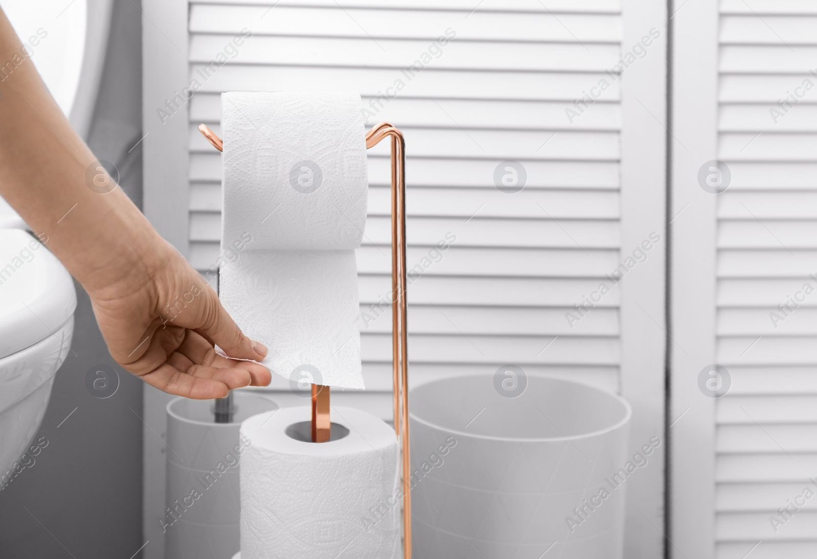 Photo of Woman taking toilet paper from roll holder in bathroom, closeup