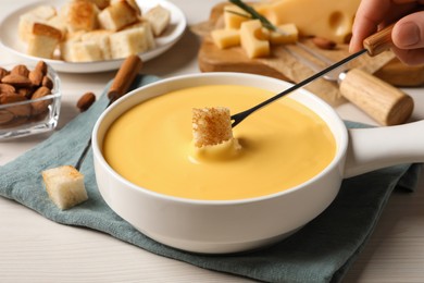 Woman dipping piece of bread into tasty cheese fondue at white wooden table, closeup