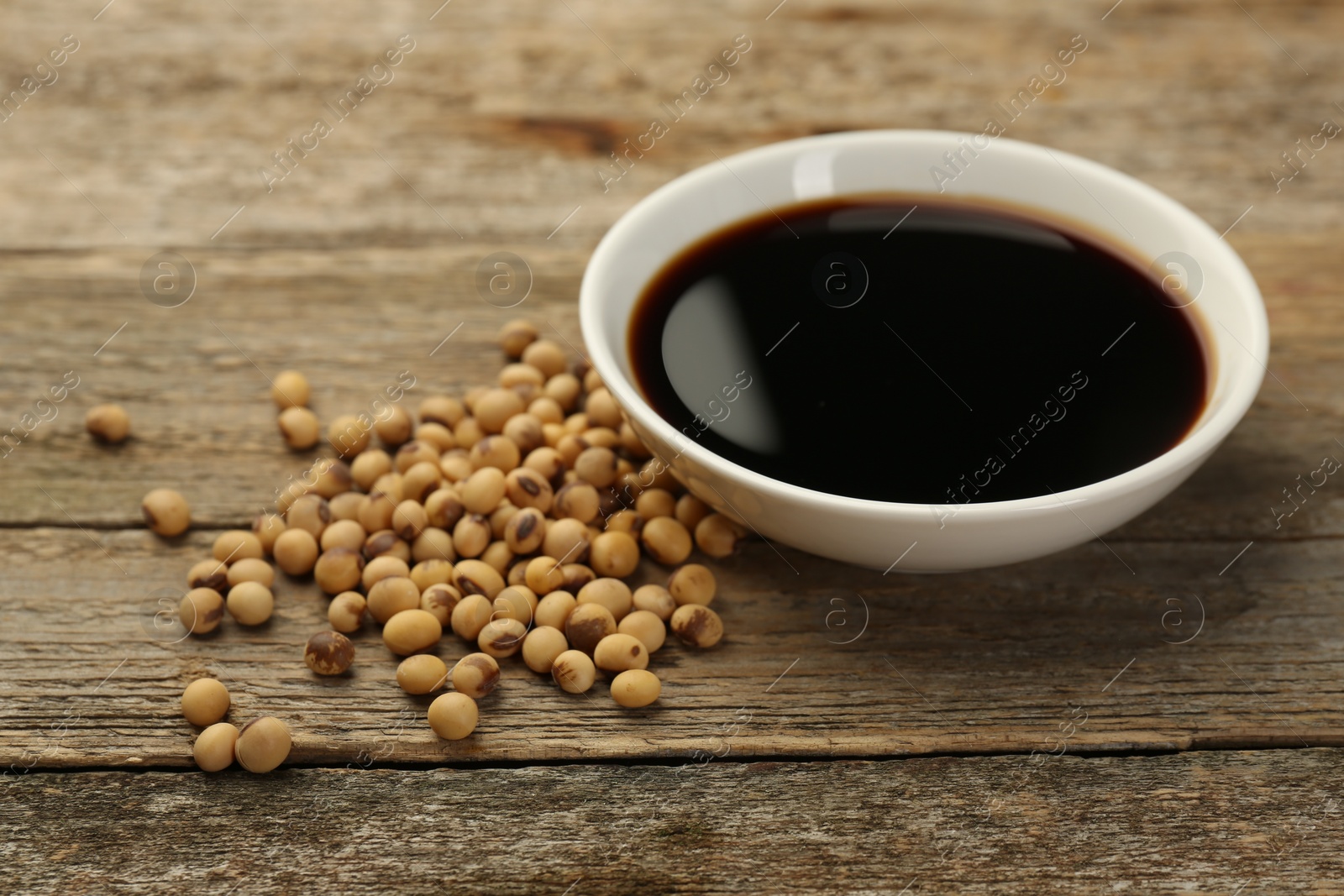 Photo of Soy sauce in bowl and beans on wooden table, closeup