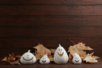 Photo of Jack-o-Lantern holders and autumn leaves on table against wooden background, space for text. Halloween decor