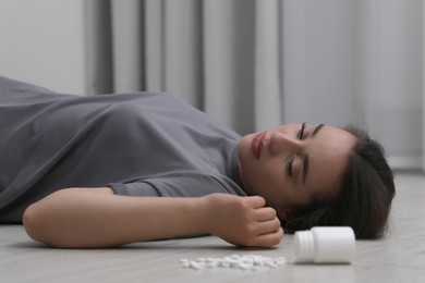Photo of Depressed woman lying on floor near overturned bottle with antidepressants indoors