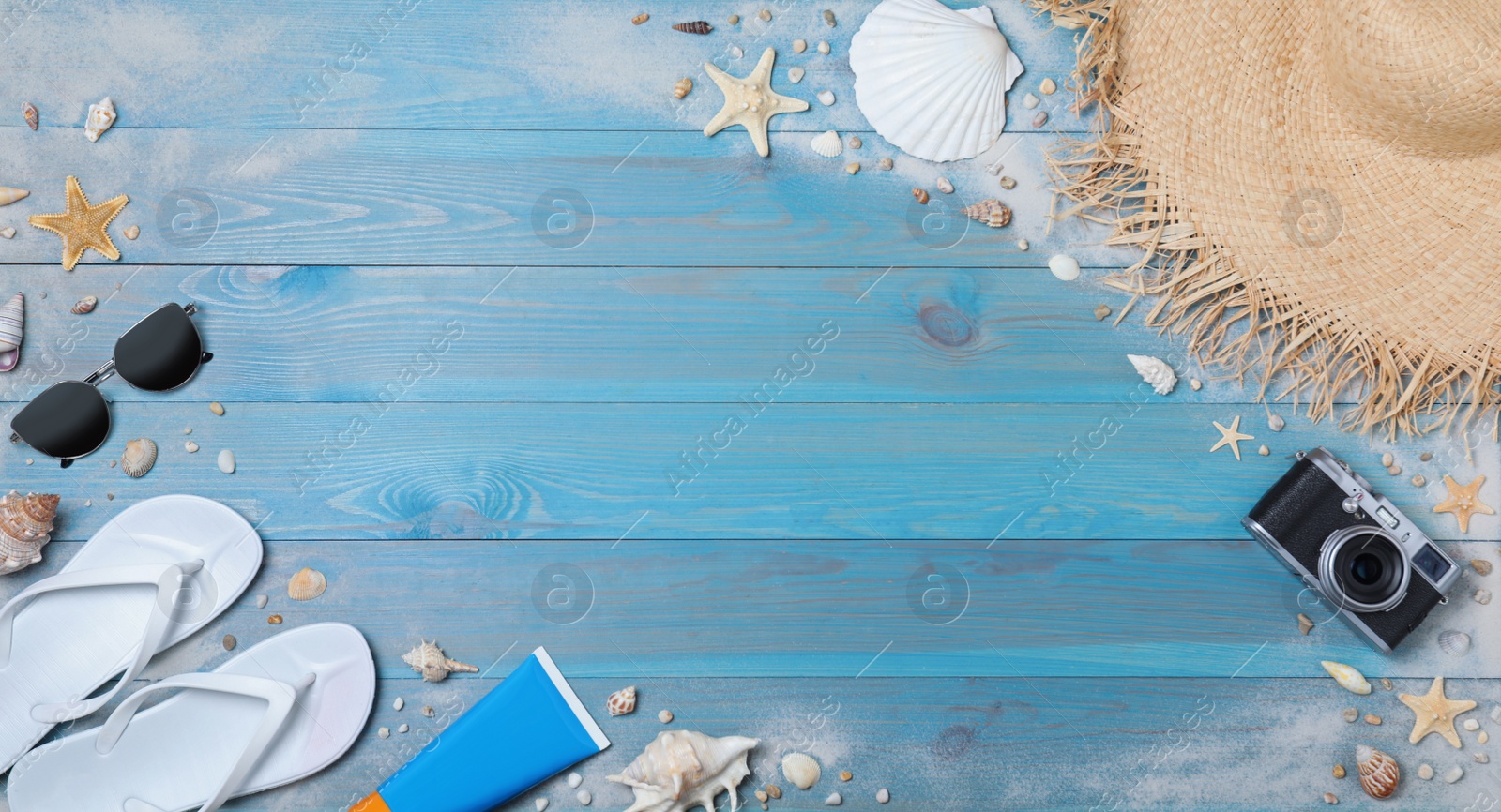 Photo of Many different flip flops and beach objects on light blue wooden background, flat lay. Space for text