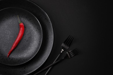 Photo of Stylish table setting. Plates, cutlery and red chilli pepper on black background, top view with space for text