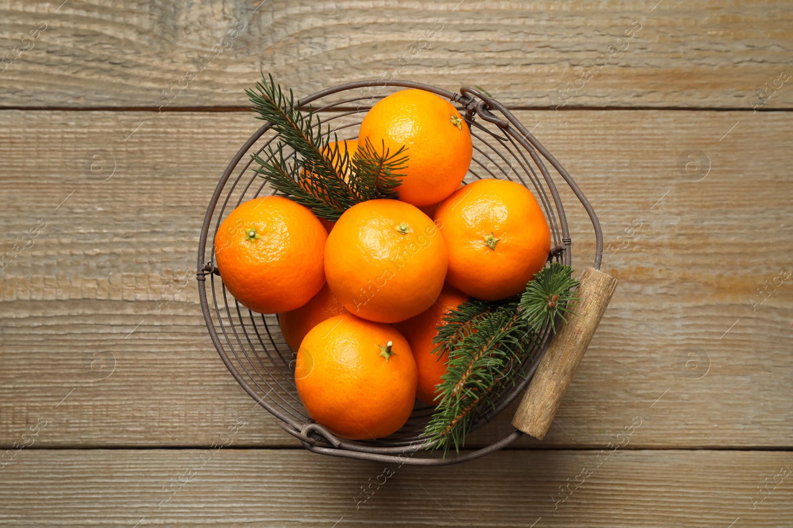 Photo of Fresh tangerines with fir tree branches in metal basket on wooden table, top view. Christmas atmosphere