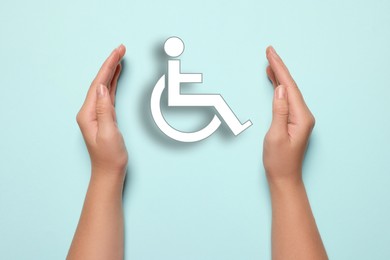 Image of Disability inclusion. Woman protecting wheelchair symbol on light blue background, closeup