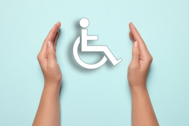 Disability inclusion. Woman protecting wheelchair symbol on light blue background, closeup