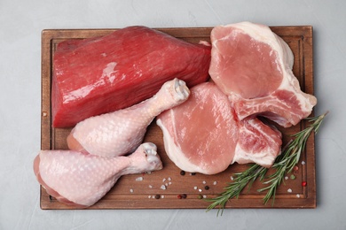 Wooden board with fresh raw meat, rosemary and spices on gray background, top view