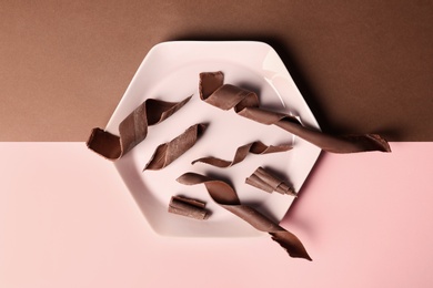 Plate with chocolate curls on color background, top view