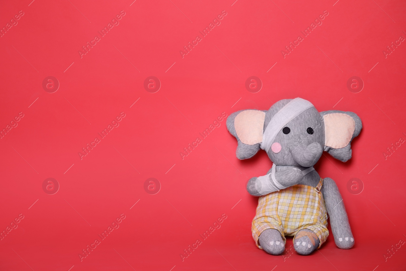 Photo of Toy elephant with bandages on red background. Space for text