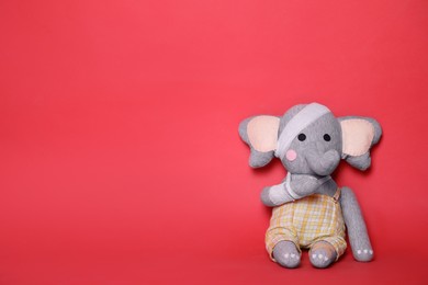 Photo of Toy elephant with bandages on red background. Space for text