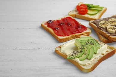 Slices of bread with different toppings on white wooden table