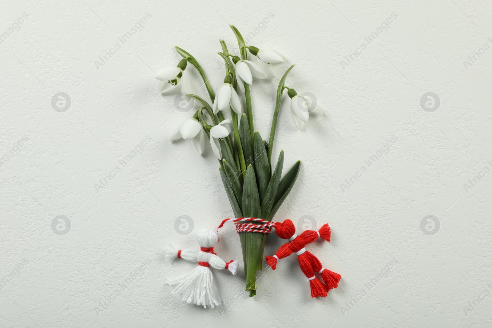 Photo of Beautiful snowdrops with traditional martisor on white background, flat lay. Symbol of first spring day