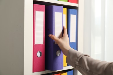 Woman taking binder office folder from shelving unit indoors, closeup