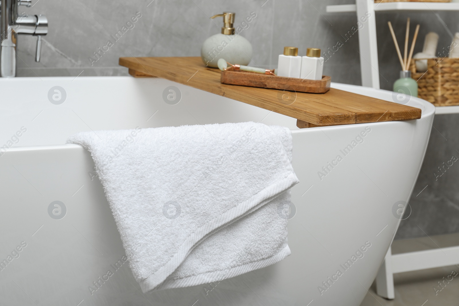 Photo of Soft bath towel and personal care products on tub tray in bathroom