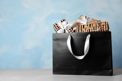 Photo of Paper shopping bag with handles full of gift boxes on table. Mock up for design