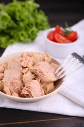 Bowl with canned tuna with fork on black wooden table, closeup