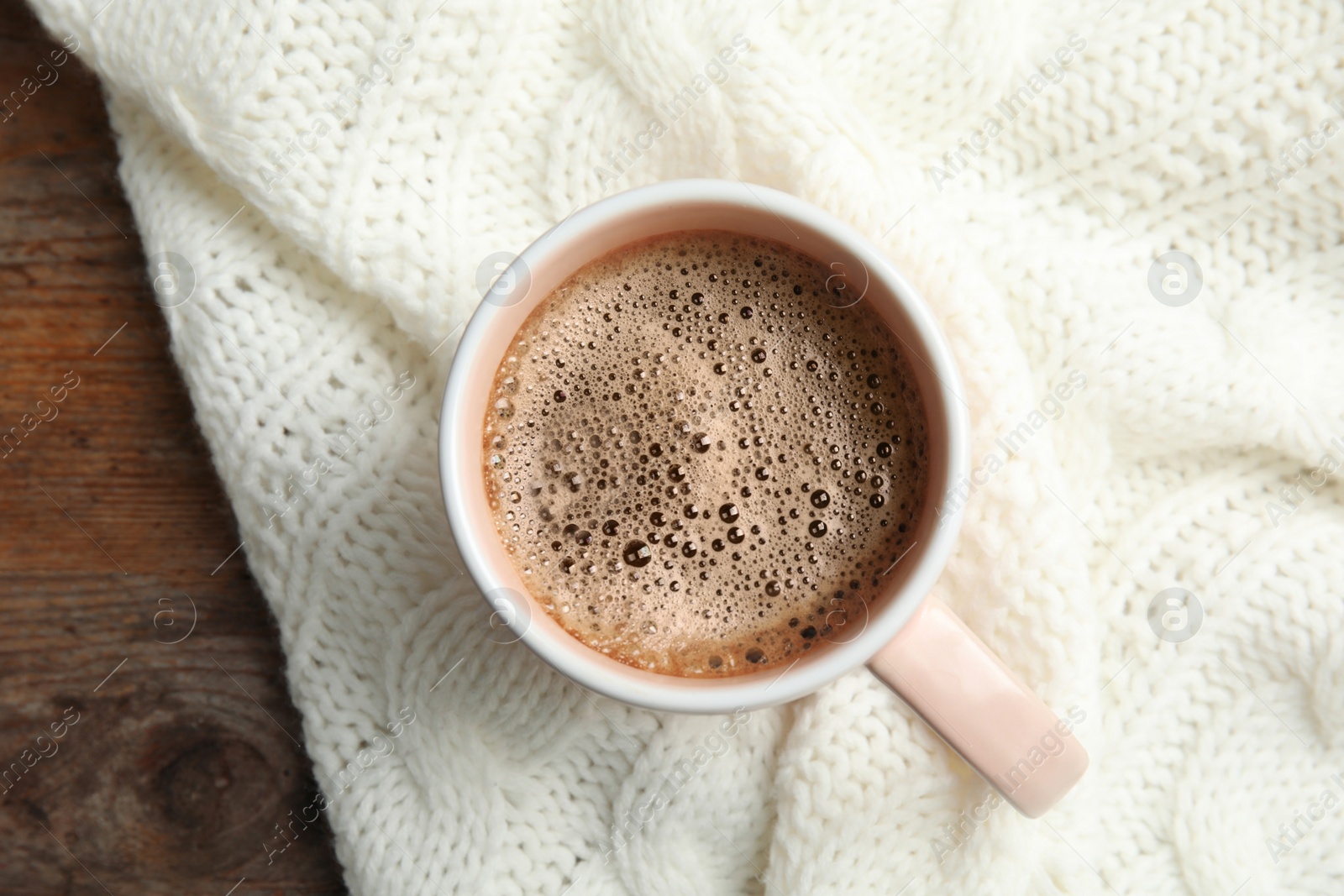 Photo of Cup of hot winter drink and knitted plaid on table, top view. Cozy season