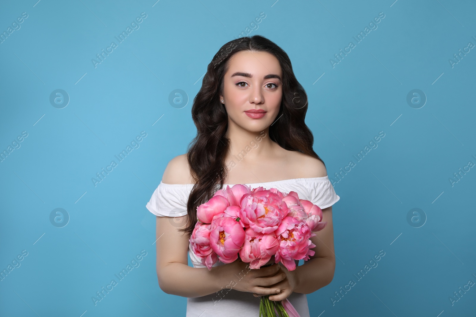 Photo of Beautiful young woman with bouquet of pink peonies on light blue background