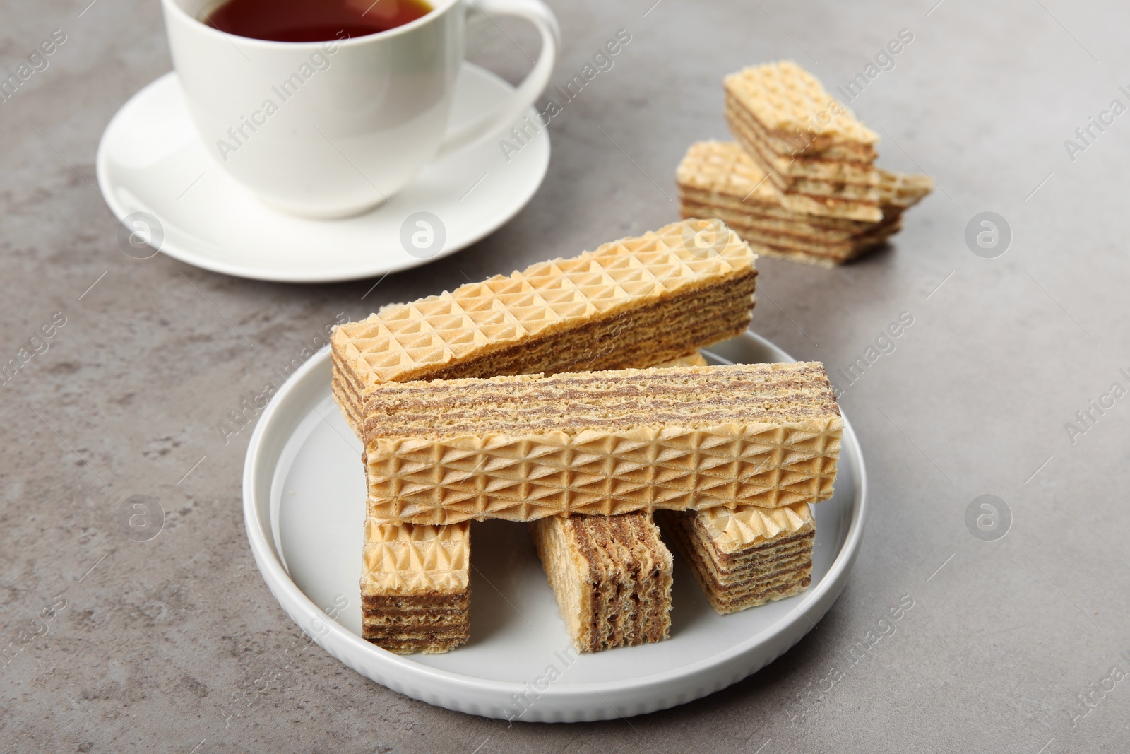 Photo of Plate of delicious wafers with cup of tea on grey stone background