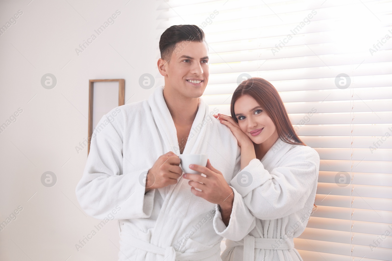 Photo of Happy couple wearing bathrobes near window at home