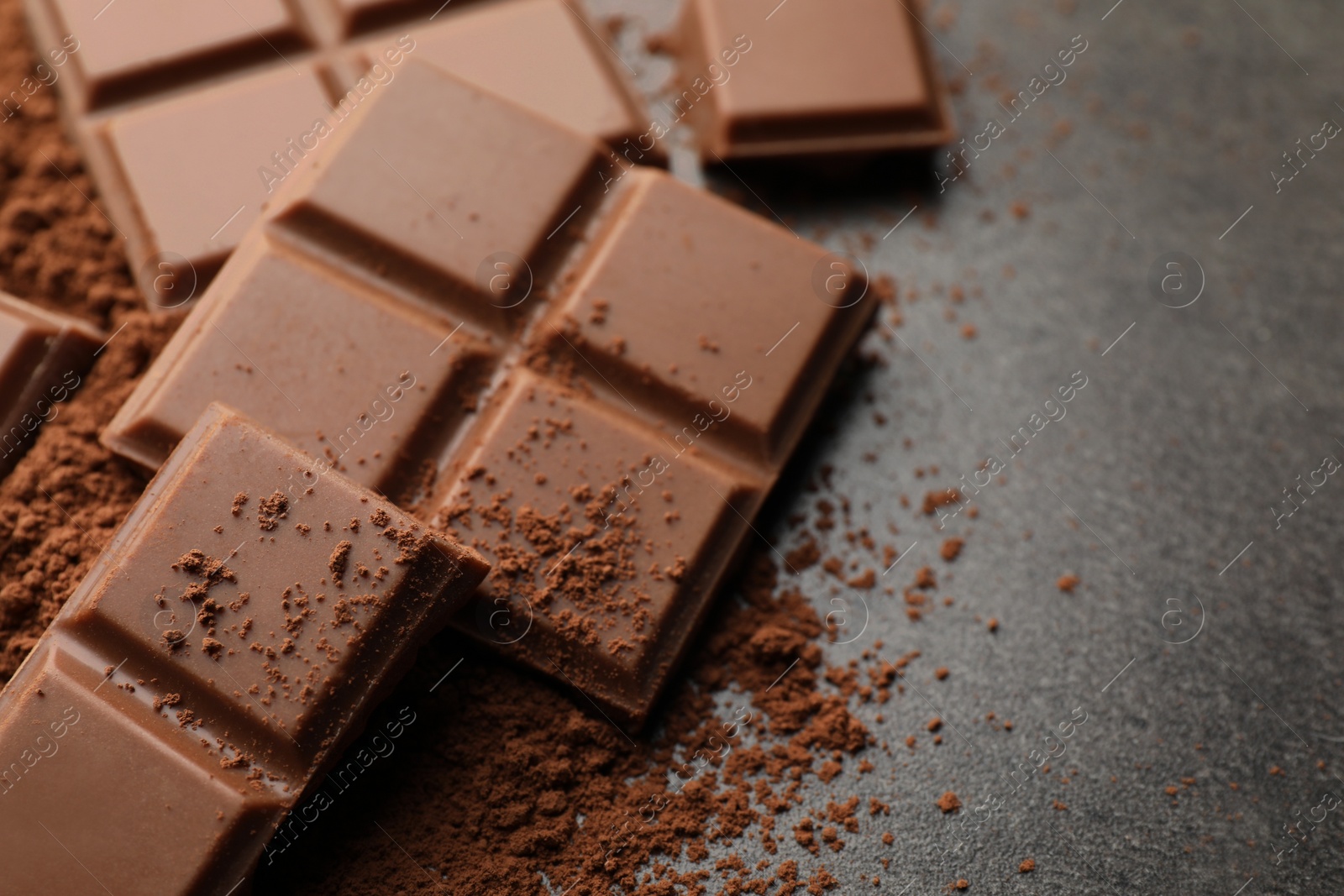 Photo of Delicious milk chocolate and cocoa powder on grey table, closeup