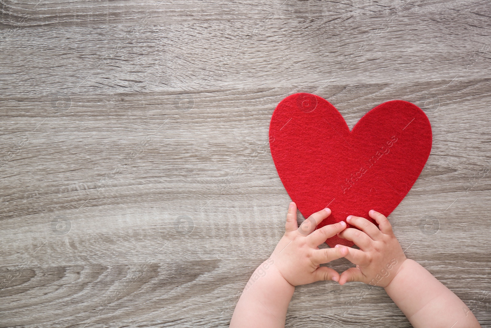 Photo of Little child's hands near red heart on wooden background, top view