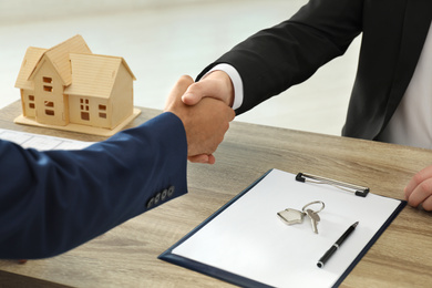 Photo of Real estate agent shaking hands with client at table in office, closeup
