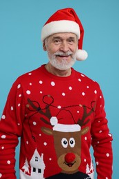 Photo of Happy senior man in Christmas sweater and Santa hat on light blue background