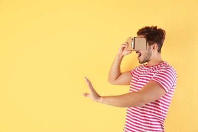 Photo of Young man using cardboard virtual reality headset on color background. Space for text