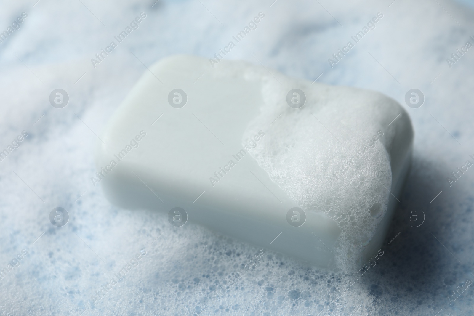 Photo of Soap with fluffy foam on light blue background, closeup