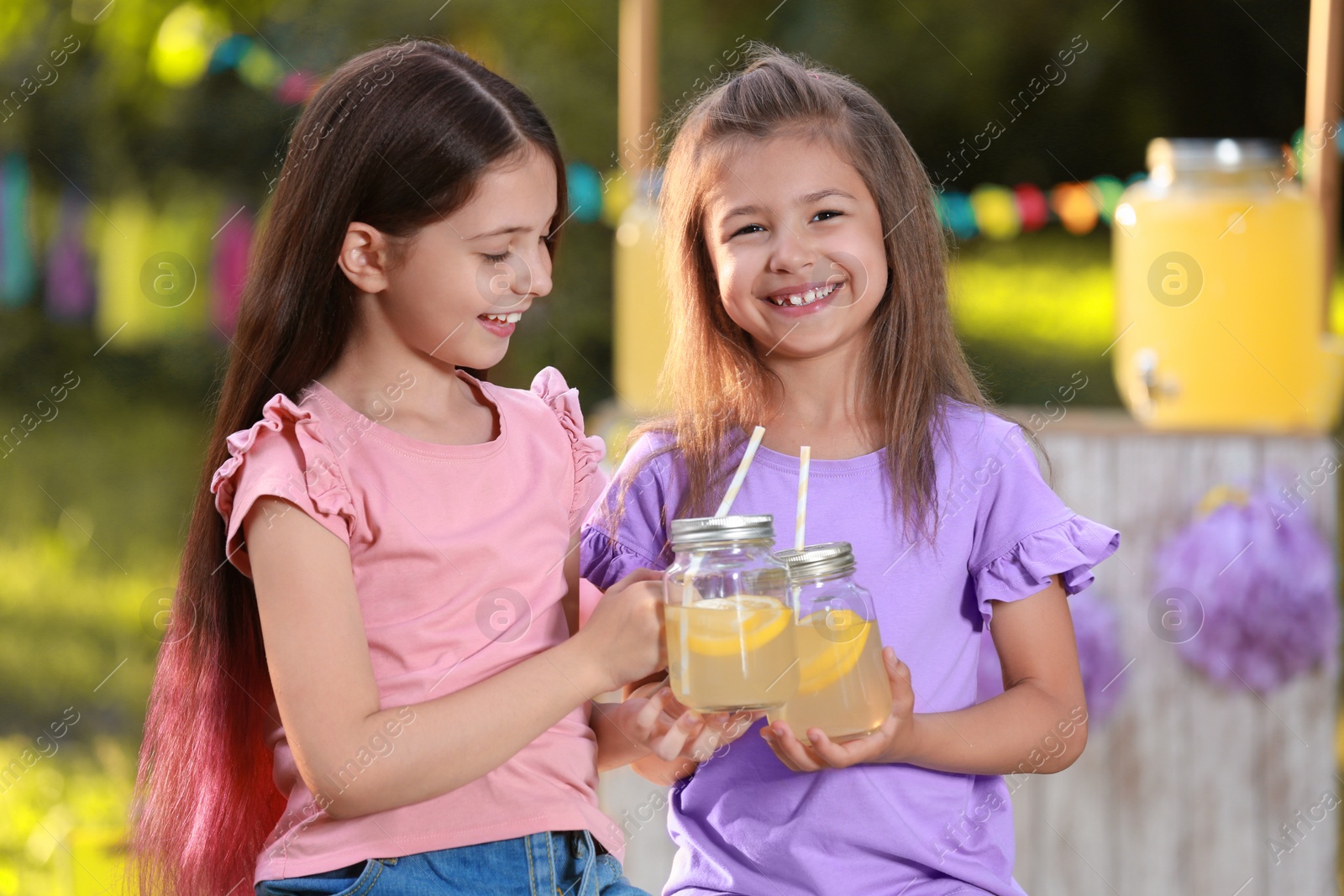 Photo of Cute little girls with natural lemonade in park. Summer refreshing drink